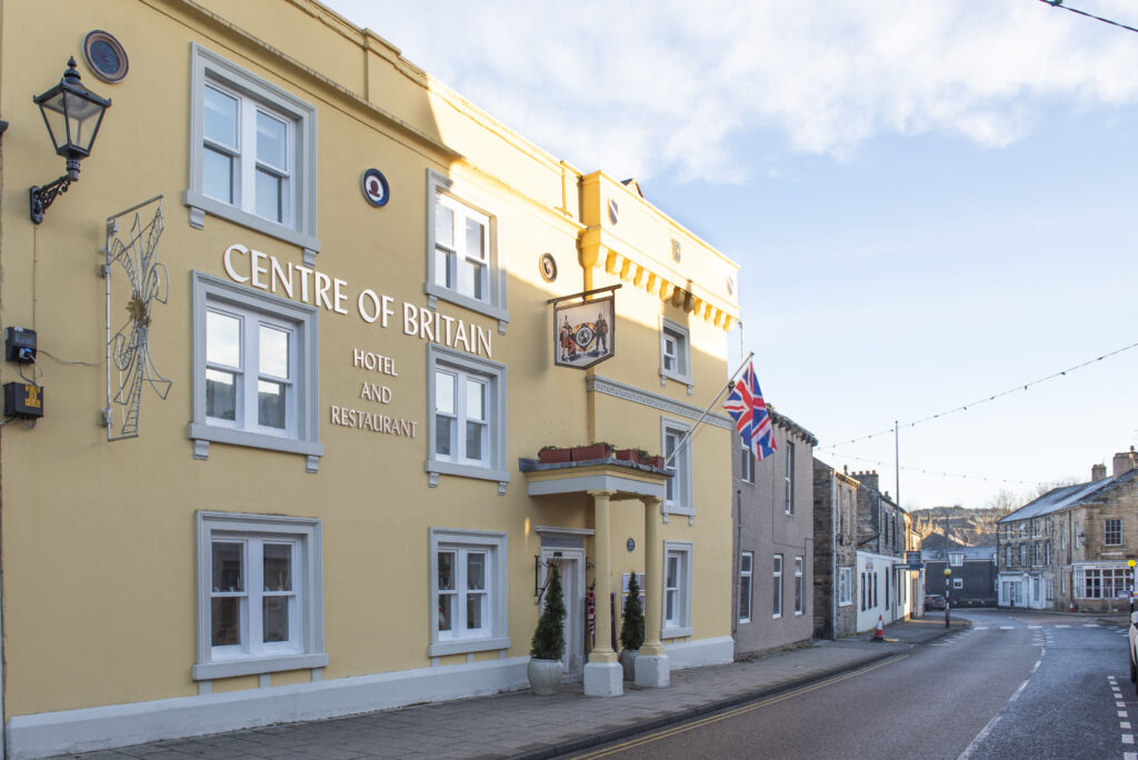 The Centre of Britain Hotel and Restaurant, a prominent yellow-painted building with Union Jack flags on a quiet street in a small English town.